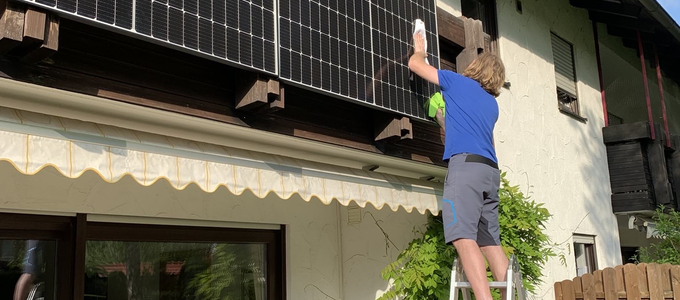 Ein Mann steht auf einer Leiter und montiert eine Solar-Anlage am Balkon | © Stadt Geretsried