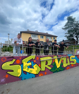 Streetart | © Stadt Geretsried Gruppe mit Bürgermeister steht vor dem Graffiti-Schriftzug "Servus" | © Stadt Geretsried