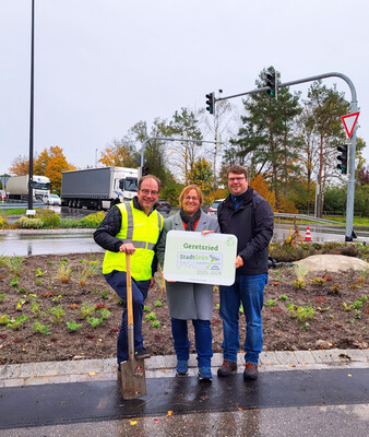 Die Gruppe steht vor der Verkehrsinsel und hält das Label StadtGrün naturnah in Silber | © Stadt Geretsried