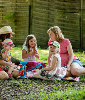 Zwei Frauen und drei Kinder sitzen unter Bäumen auf der Wiese | © Bernd Ritschel