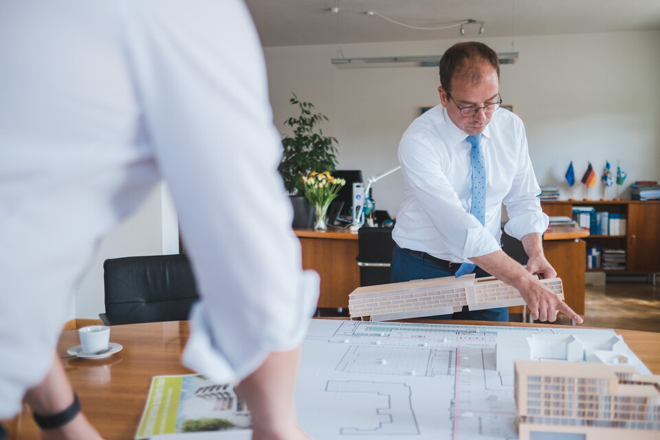 Erster Bürgermeister Michael Müller blickt auf Baupläne und hält ein Modell eines Gebäudes in der Hand | © Stadt Geretsried